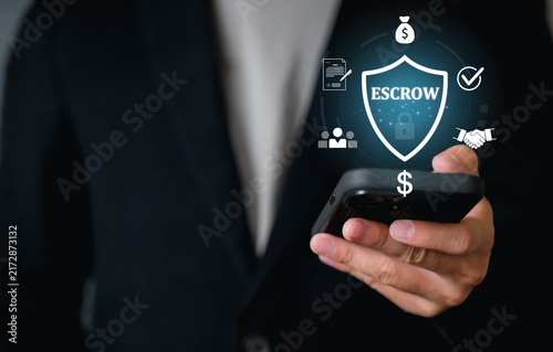 A person in business attire holds a smartphone with Escrow. This refers to money, deposits, or assets deposited with a third party as collateral, security services, and financial transactions.