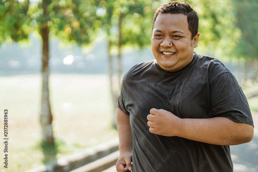 Fototapeta premium portrait of an overweight man with a smile while jogging in the morning at the park