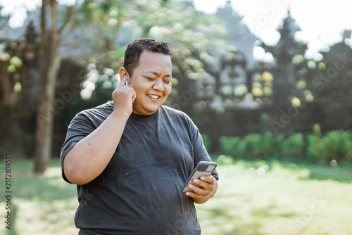 fat man wears hands free when listening to music using cell phone when going to exercise