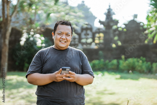 fat man smiles wearing handfree and holding cell phone after exercise in the park