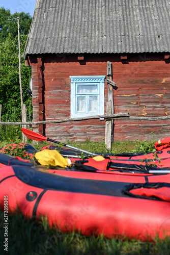 Red packrafts resting on grass in front of old rustic wooden house with blue window frame.