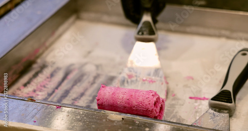 фотографія Pink berry ice cream roll being prepared with metal spatula on frozen plate, traditional Thai street food dessert making process, commercial kitchen background