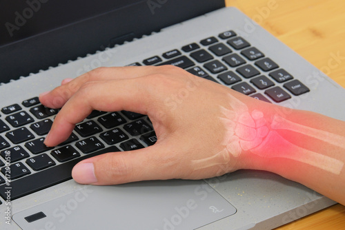Wrist pain showing a worker using a computer keyboard with highlighted wrist anatomy for carpal tunnel and repetitive strain treatment concepts.