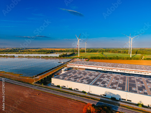 Industrial solar farm and rooftop panels. Solar energy installations cover rooftops and farmland adjacent to a asphalt highway.
