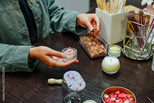 Participants work together at a candle making master class, using jars, wicks, wax pieces, tools, brushes, and decorative materials around a wooden table