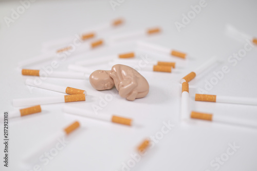 Foto Model of human fetus lies among a pile of cigarettes in pregnant woman addiction closeup