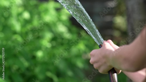 The teenagers hands are holding the hose, watering the vegetation in the yard of their house.