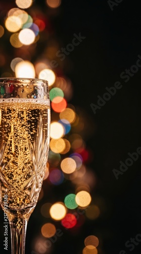 Crystal flute holding sparkling for a festive toast. Blurred bokeh lights create a magical atmosphere for the new year.