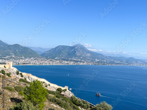 Scenic high angle view of the historic Alanya castle walls on a hill slope with a pirate ship sailing in the Mediterranean sea, Turkey