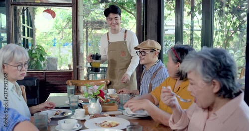 Senior Asian women friends reunion at restaurant table, retired female group receiving drink service from young waiter, sharing brunch conversation, togetherness, social dining, cafe lifestyle moment