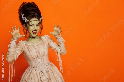 Woman in Bride of costume with spooky makeup and dress, Halloween orange background with copy space