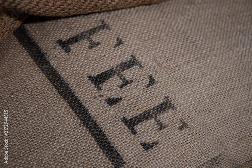 Close-up of the rough woven texture of an old burlap cargo sack with black stenciled letters used for import and export transport.