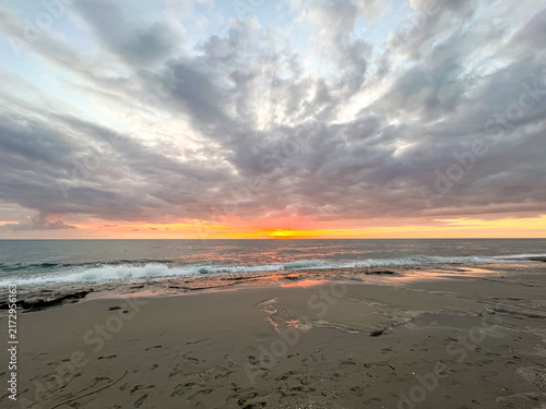 Scenic view of a dramatic golden sunset over a sandy sea beach with textured storm clouds in the sky