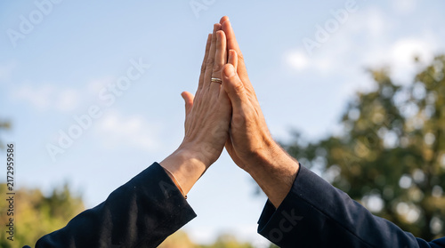 Two hands giving a high five outdoors with blue sky and natural background, symbolizing teamwork, friendship, partnership, success and celebration.