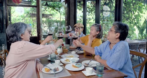 Senior Asian women celebrating reunion at restaurant with red wine toast, retired female group smiling over brunch, sharing laughter, companionship, social connection, joyful lifestyle moment