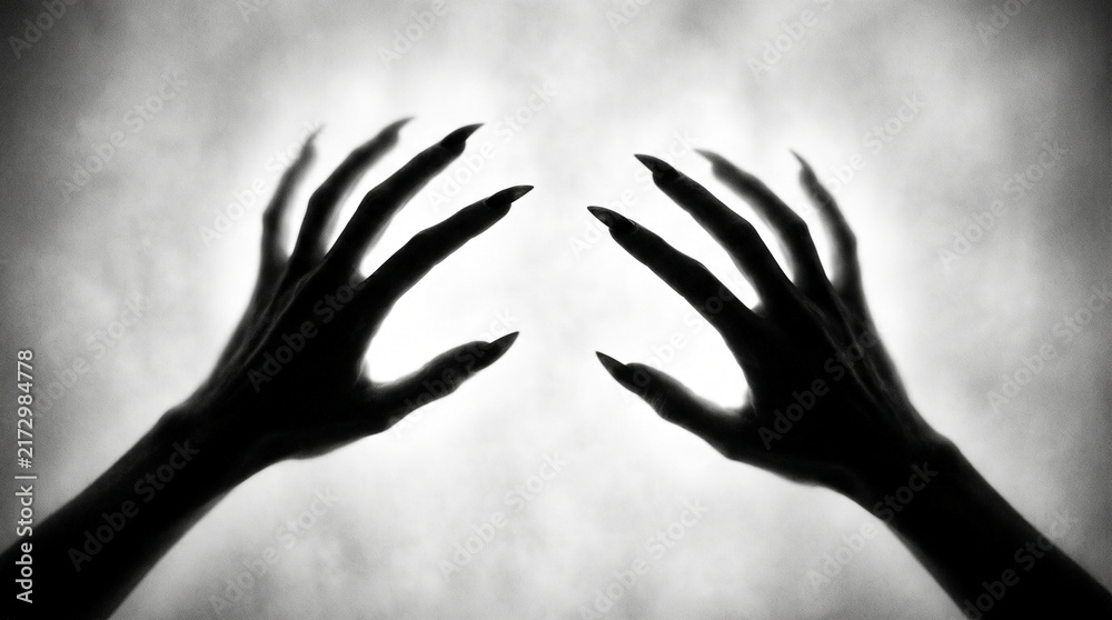 Obraz premium Silhouette of two clawed hands reaching out with sharp nails against a foggy, bright background, symbolizing mystery and horror