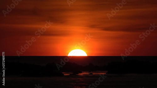 Bright sun setting over dark water horizon at dusk or dawn