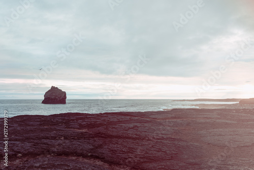 Fotografía Karlinn sea stack rises from luminous water while sunlight cuts through coastal haze at Valahnukamol on the Reykjanes Peninsula, Iceland