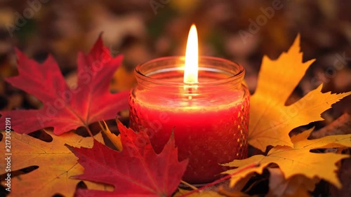 Burning candle flame surrounded by autumn leaves in warm candlelight