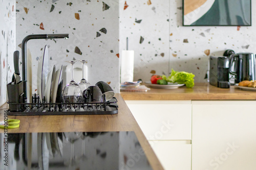 Kitchen sink area shows dish rack cooktop and fresh vegetables ready for breakfast preparation. Concept of organized kitchen workspace and morning meal prep in modern household setting.