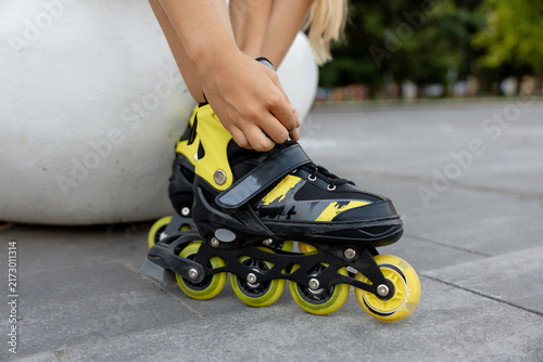 Close-up of teenager girl fastening yellow and black inline skates outdoors 