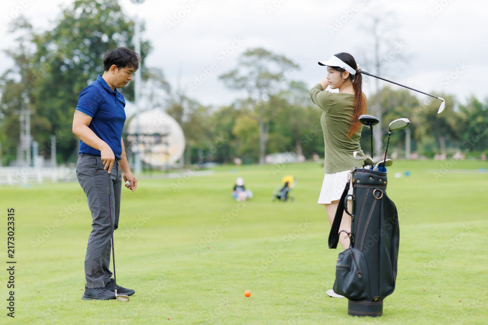 Obraz premium Coach teaching woman golf swing technique at driving range, male trainer giving individual instruction during golf lesson, female trainee practicing outdoor sport