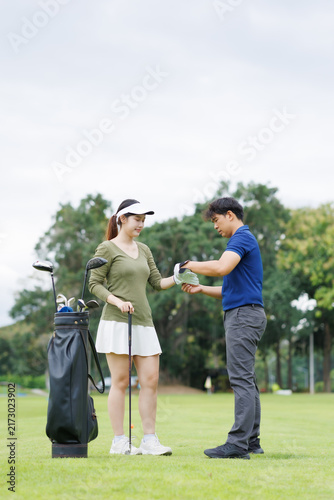 Bild auf Leinwand Golf instructor helps woman put on golf glove on lush course, teaching grip and
