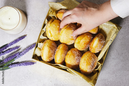 Hand Reaching for Sugar-Coated Donuts in Decorative Box With Candle and Lavender