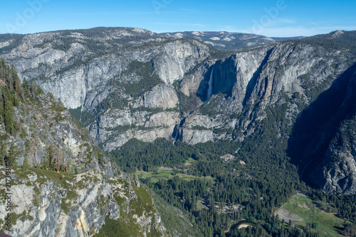 Canvas Print Aerial landscape of Yosemite Falls plunging into a forested valley framed by granite cliffs and clear blue sky, evoking grandeur and wilderness