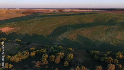 Golden hour light illuminating vast green agricultural fields and rolling hills. An aerial drone flying over a beautiful rural landscape at sunset, showcasing the scenic countryside beauty