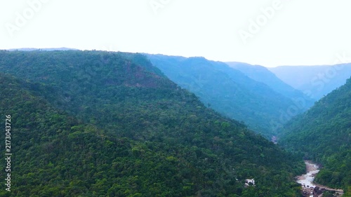 Dramatic Khasi Hills landscape with winding Piyain River beneath hazy sky at Meghalaya - Aerial panning shot.