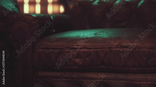 A leather couch sits in a dark room. There is a green light reflecting off the surface. The atmosphere feels cozy and inviting, making it a good spot for sitting and relaxing.