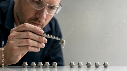 Focused man using tweezers to arrange metal nuts on white surface demonstrating precision and concentration