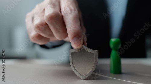 Close up of hand holding shield protecting green pawn symbolizing security and protection concept