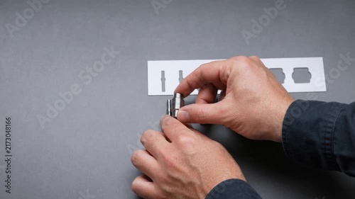 Close up of hands inspecting and comparing small metal mechanical parts on gray surface with blueprint