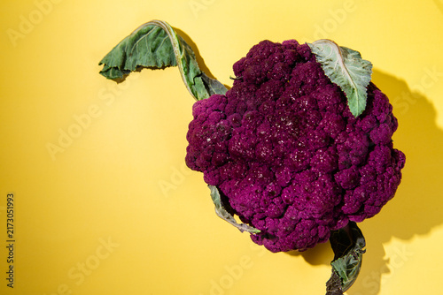 Cuadro en lienzo Fresh purple cauliflower head with green leaves on bright yellow background