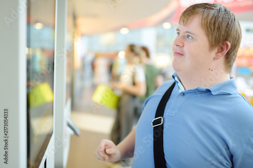 Portrait of a teenager with Down syndrome in a big city. Boy with Down syndrome chooses food on interactive screen in fast food restaurant