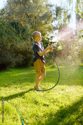 Photography Funny preteen boy pouring cool water on himself and playing with garden hose with sprinkler in sunny backyard