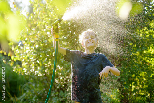 Photography Funny preteen boy pouring cool water on himself and playing with garden hose with sprinkler in sunny backyard