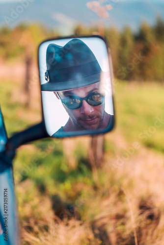 Reflection in rear-view mirror of man wearing a hat and sunglasses