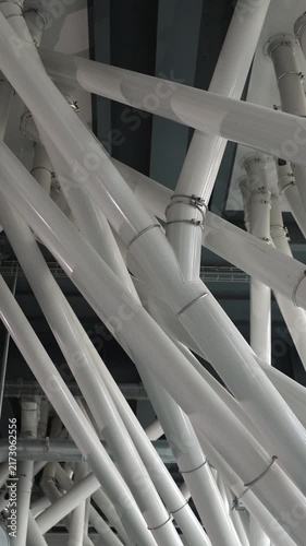 Vertical video. Intricate network of white pipes and metal tubes inside a modern industrial flour mill, showcasing the complex machinery and automated system for grain processing and food production