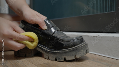 Canvas Print Close up hands uses a yellow sponge to wipe a black loafer for cleaning