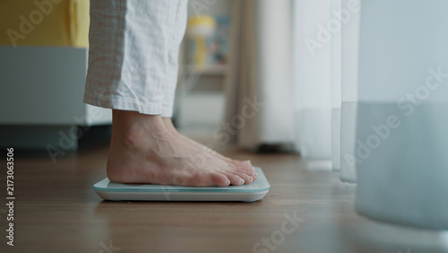 Quadro su tela A person in white pajamas standing barefoot on a digital weight scale placed on