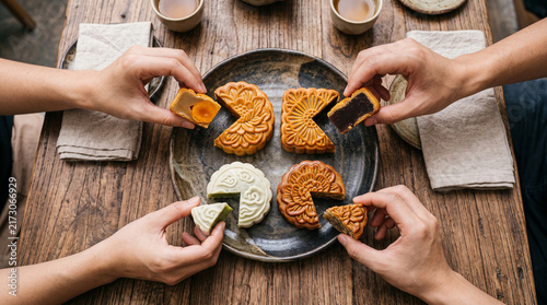 Close up of  four hands holding sliced cut of mooncake with egg yolk for Chinese Mid-Autumn Festival