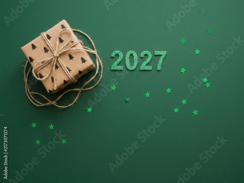 Festive 2027 new year background with a wrapped gift box and green glitter numbers on a dark green surface