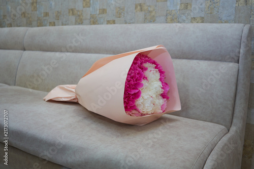 Bouquet of pink and white peonies on a beige sofa, Beautiful festive floral bouquet of peonies in peach wrapping paper lying on a sofa