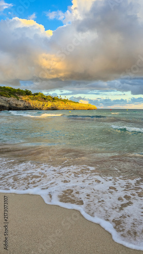 Sandy beach with sea foam at sunset in Cala Mendia