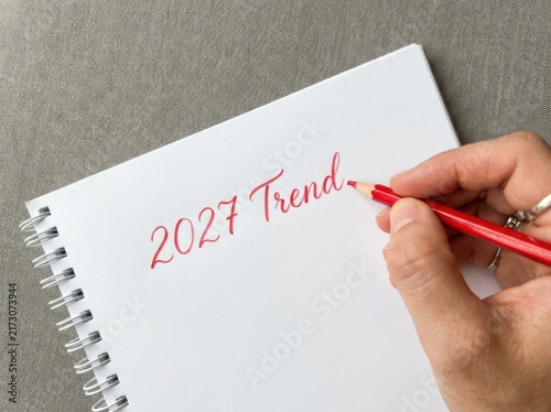 Close up of a hand writing 2027 trend in a spiral notebook with a red pencil