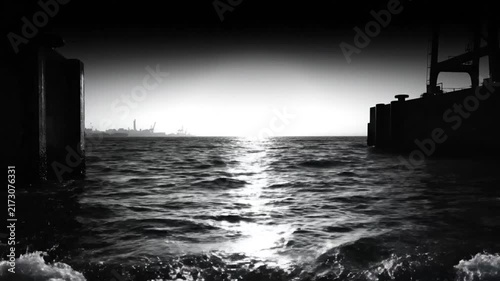 Dramatic black and white seaside scene capturing choppy water and industrial landscape in a cinematic composition