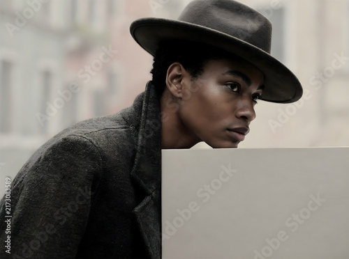 Mysterious portrait of a stylish woman in a wide-brimmed hat and overcoat against an urban backdrop